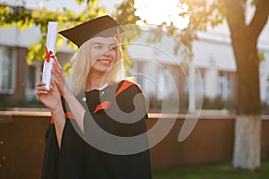 Portrait enthusiastic female college student graduate in cap and gown celebrating, holding diploma.