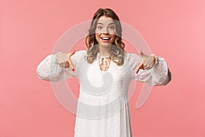 Portrait of enthusiastic upbeat young blond woman pointing fingers down to invite you check-out product, showing bottom