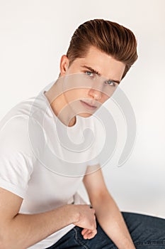 Portrait European attractive young man with stylish hairstyle with clean skin in fashionable classic white t-shirt in blue vintage