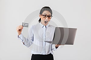 Portrait of european businesswoman wearing eyeglasses holding silver laptop and credit card in the office, isolated over white