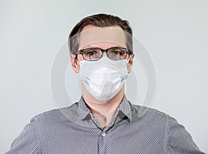 Portrait of an European one man in glasses and one-use mask, looking at camera, grey background