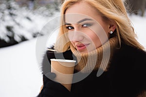 Portrait of european style fashionable woman drinking coffee in winter park.