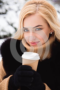 Portrait of european style fashionable woman drinking coffee in winter park.