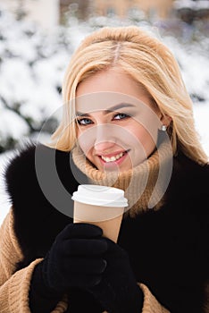 Portrait of european style fashionable woman drinking coffee in winter park.