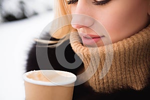 Portrait of european style fashionable woman drinking coffee in winter park.