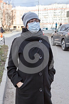Portrait of an European woman in glasses and one-use mask, looking at camera standing outdoor