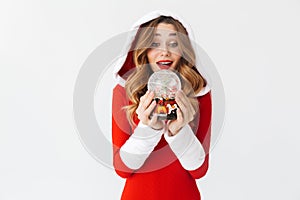 Portrait of european woman 20s wearing Santa Claus red costume smiling and holding Christmas snow ball, isolated over white