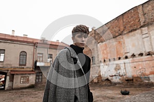 Portrait of a European young man in stylish classic outerwear with a fashionable hairstyle walks along a city street near old