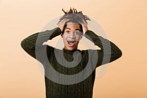 Portrait of excited african american man yelling and grabbing head, isolated over beige background