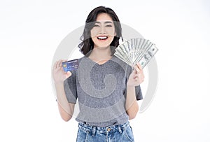 Portrait of an excited Asian woman holding bunch of money banknotes and showing credit card isolated over white background.