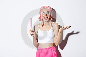 Portrait of excited beautiful girl dressed up as fairy on halloween, wearing pink wig and bright makeup, holding candle