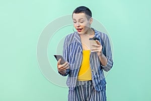 Portrait of excited beautiful with short hair young blogger woman in striped suit standing, reading interesting news and drink