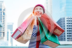 Portrait of an excited beautiful young girl wear shirt and wool hat holding many shopping bags and smile. With copy space.