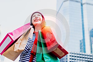 Portrait of an excited beautiful young girl wear shirt and wool hat holding many shopping bags and smile. With copy space.