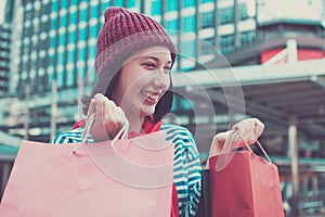 Portrait of an excited beautiful young girl wear shirt and wool hat holding many shopping bags and smile. With copy space.