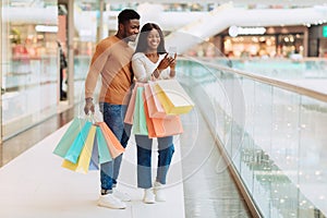 Portrait of excited black spouses using phone in shopping mall