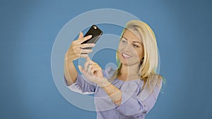 Portrait of excited cheerful smiling young pretty woman making selfie photo on smartphone. Solid background.