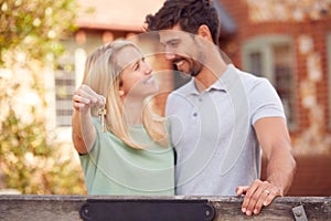 Portrait Of Excited Couple By Gate Holding House Keys Outside New Home In Countryside On Moving Day