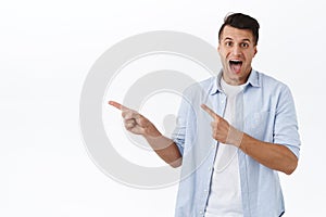 Portrait of excited, enthusiastic handsome man pointing fingers left and smiling amazed, found excellent promo, best