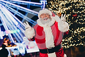 Portrait of excited funky santa grandfather two hands fingers demonstrate v-sign enjoy newyear time lights outdoors