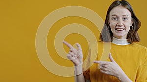 Portrait of excited girl pointing sidewards recommending smiling on yellow background