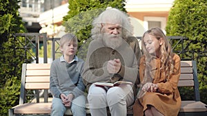 Portrait of excited grandfather gesturing and talking with cheerful grandchildren outdoors. Happy intelligent senior