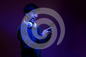 Portrait of excited handsome young asian man looking at the mobile phone wearing headphone in neon light