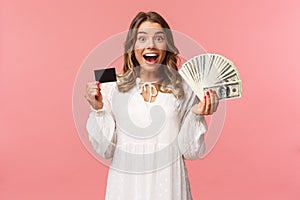 Portrait of excited happy good-looking blond girl in white dress, winning money, placed good bet, made deal, holding