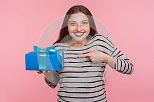 Portrait of excited happy young woman in striped sweatshirt pointing at birthday gift and smiling to camera photo