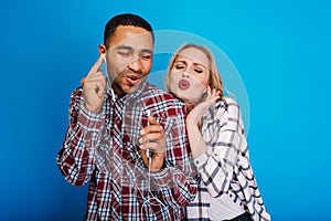 Portrait excited joyful couple listening to music through headphone on blue background. Having fun, singing with closed