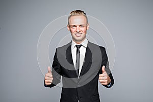 Portrait of excited man with opened mouth dressed in formal wear giving thumbs-up against gray