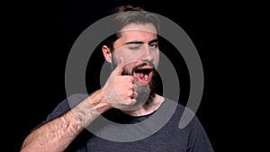 Portrait of excited man with opened mouth giving thumbs-up and winking against black background. Smiling bearded young