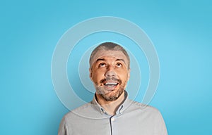 Portrait Of Excited Mature Man Looking Up Over Blue Background