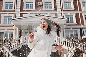 Portrait excited playful girl having fun with snow in frozen sunny morning on street. True emotions, laughing with