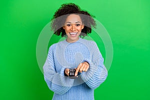 Portrait of excited positive lady arms hold remote control press power button isolated on green color background