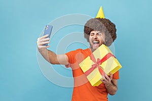 Portrait of excited positive man holding gift box and making selfie or video call.