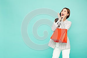 Portrait of excited screaming young asian woman holding shopping bag isolated over green background.