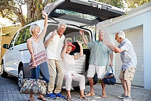 Portrait Of Excited Senior Friends Loading Luggage Into Trunk Of Car About To Leave For Vacation