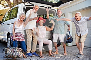 Portrait Of Excited Senior Friends Loading Luggage Into Trunk Of Car About To Leave For Vacation