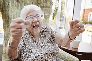 Portrait Of Excited Senior Woman Sitting In Chair In Lounge Of Retirement Home