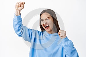 Portrait of excited smiling girl celebrating, screaming and chanting, make fist pump, looking aside rooting for team