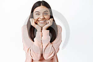 Portrait of excited smiling girl leaning on face and looking enthusiastic at camera, gazing at something with interest