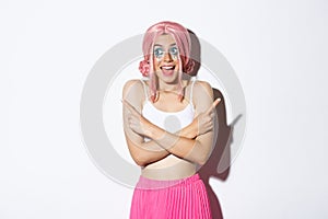 Portrait of excited smiling girl with pink wig and party makeup, pointing fingers sideways but looking left with happy