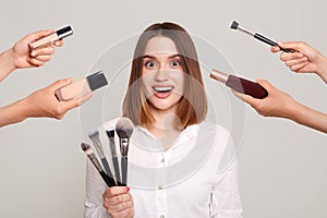 Portrait of excited surprised Caucasian woman with brushes in hands, looking at camera with ope mouth and big eyes, visiting salon