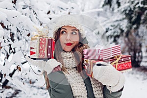 Portrait of excited woman checking Christmas presents gift boxes wrapped in festive paper in snowy winter park outdoors.