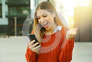 Portrait of an excited woman wearing a red sweater winning online outside on the street in autumn