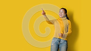 Portrait of an excited young blonde girl pointing with hand and finger to the side looking at the camera over yellow background.