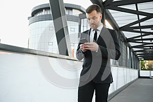 Portrait of an excited young businessman dressed in suit holding mobile phone, celebrating.