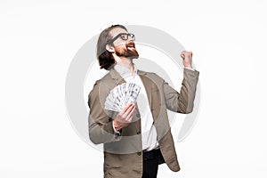 Portrait of an excited young businessman dressed in suit showing money banknotes isolated over gray background