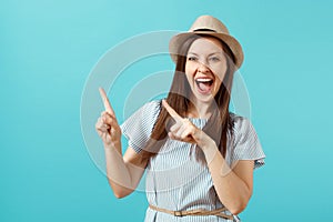 Portrait of excited young elegant woman wearing dress, straw summer hat pointing index fingers on copy space isolated on